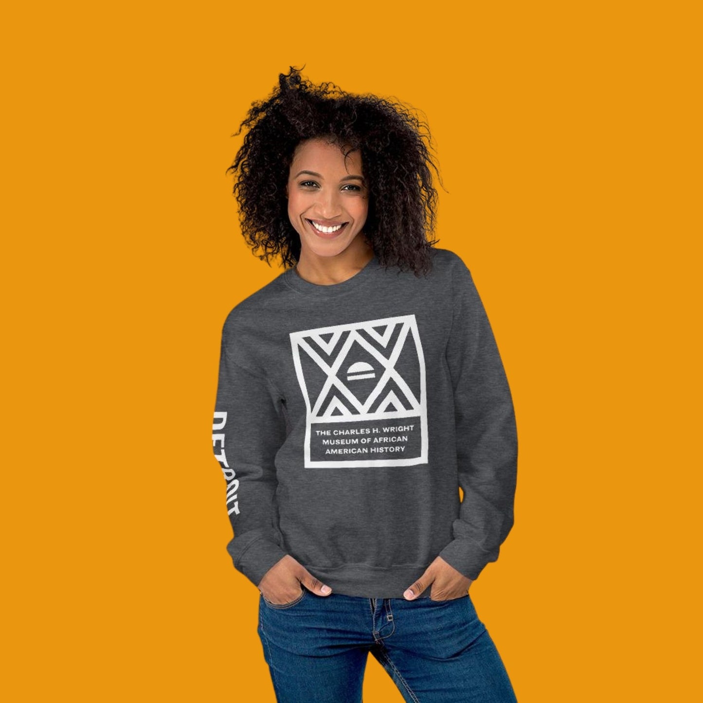 African American women posed, wearing a dark heather gray sweatshirt with the Charles H. Wright Museum logo on the front and text with DETROIT in all caps on the right sleeve.